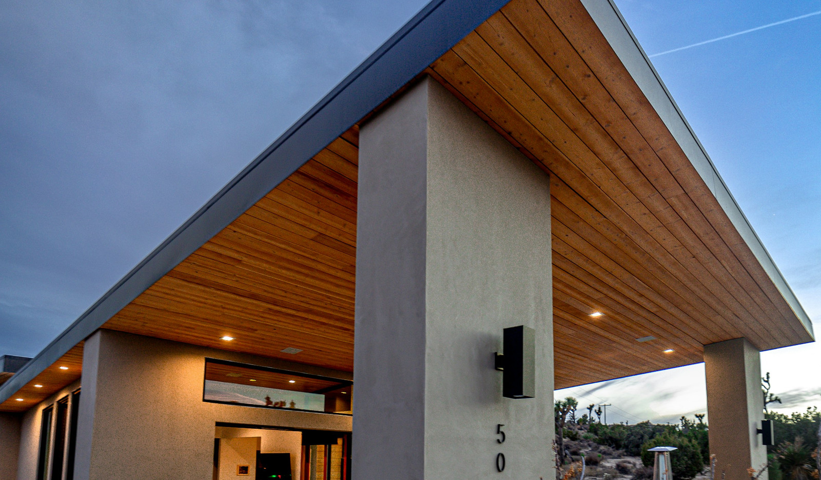 Covered outdoor area of a contemporary house, with a timber soffit running the length of the eave and recessed lighting.