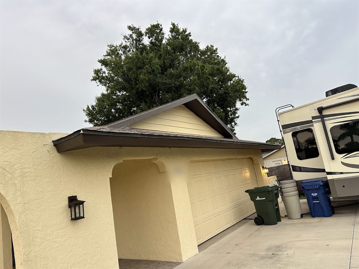 Yellow stucco home with brown fascia and soffit and a new gutter running above the garage.