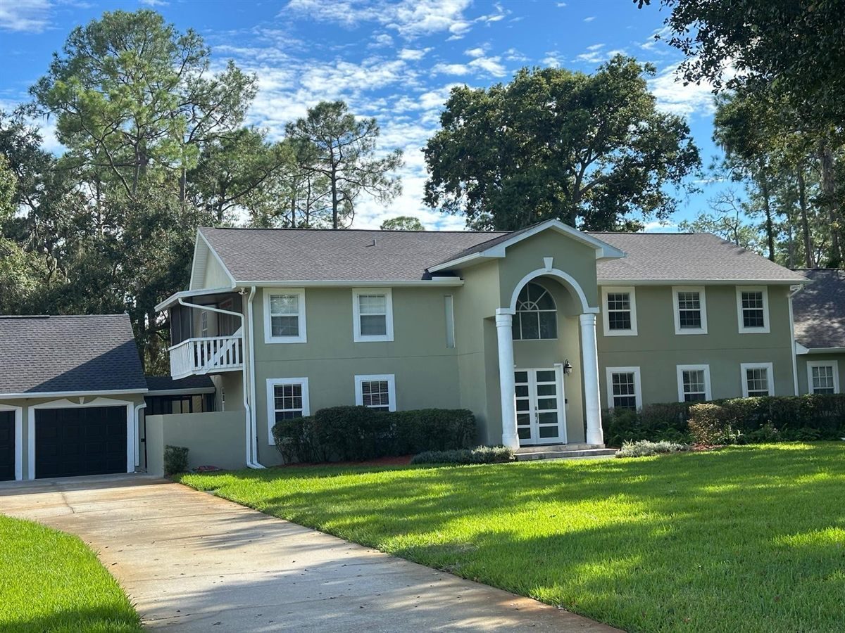 Sage green two-story home with white entry columns, new fascia and a downspout beside the garage.