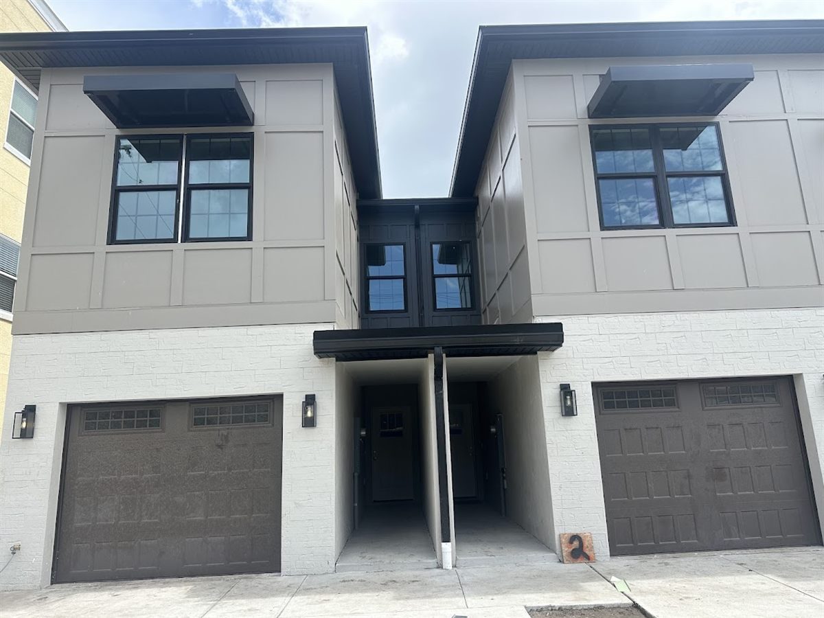 Paired new-build townhomes with dark soffit, fascia and window awnings across the front elevation.