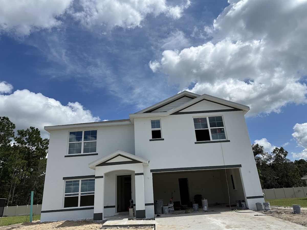New-build two-story home mid-construction, dark trim in place and the soffit line still open.