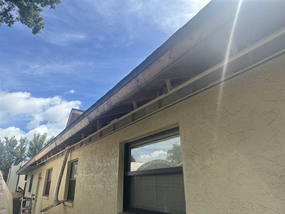 Open eave showing weathered rafter tails and darkened sub-fascia before repair.