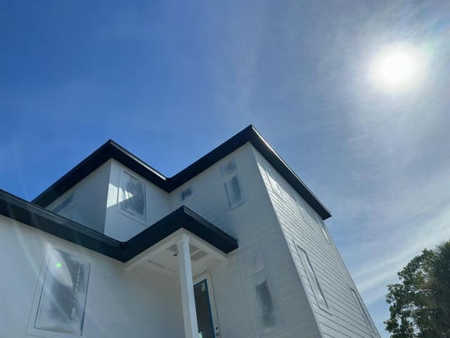 New white two-story home with black soffit and fascia, windows still film-covered.