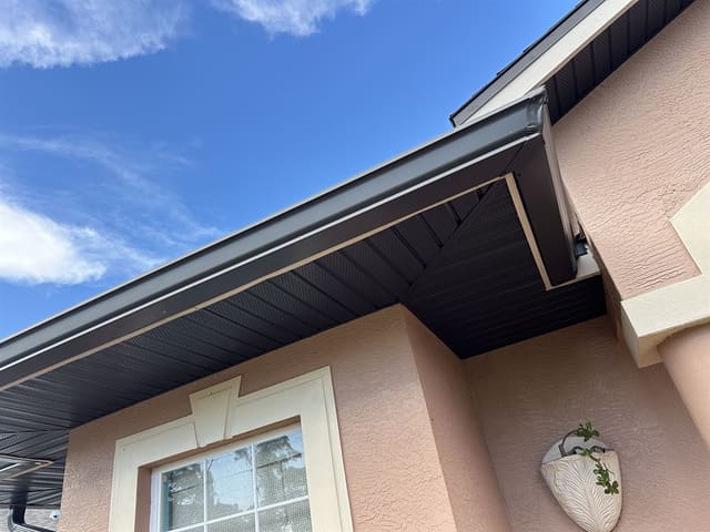 Finished bronze vented aluminum soffit and matching gutter along a stucco home's eave.