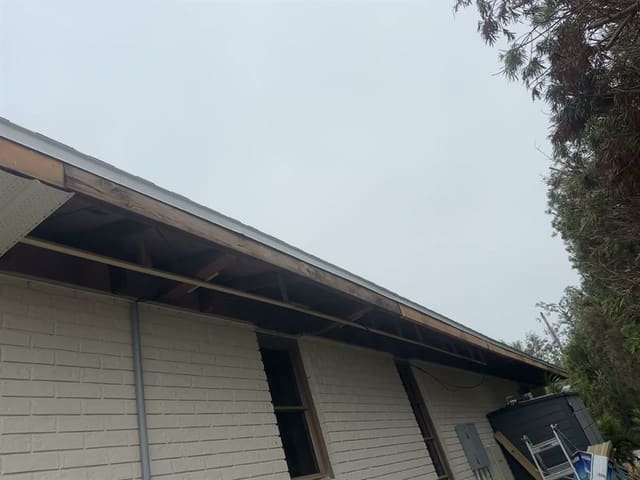Eave stripped back exposing weathered wood rafter tails and sub-fascia.