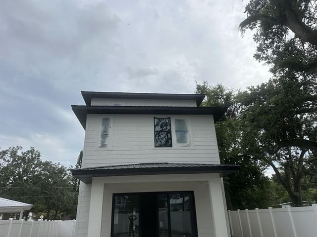 Front of a new white home with black soffit and fascia, windows still filmed.
