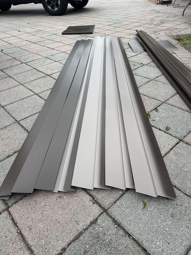 Bundle of pre-bent aluminum fascia and trim stock laid out on a paver driveway.