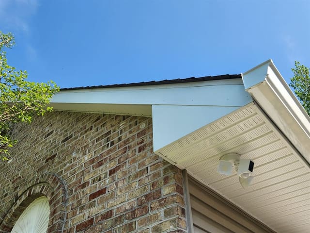 Cream vented soffit and white gutter wrapping the eave of a brick home.