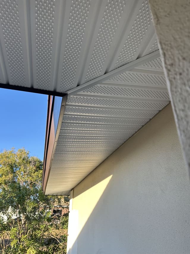 Close view of white vented aluminum soffit panels meeting a stucco wall.
