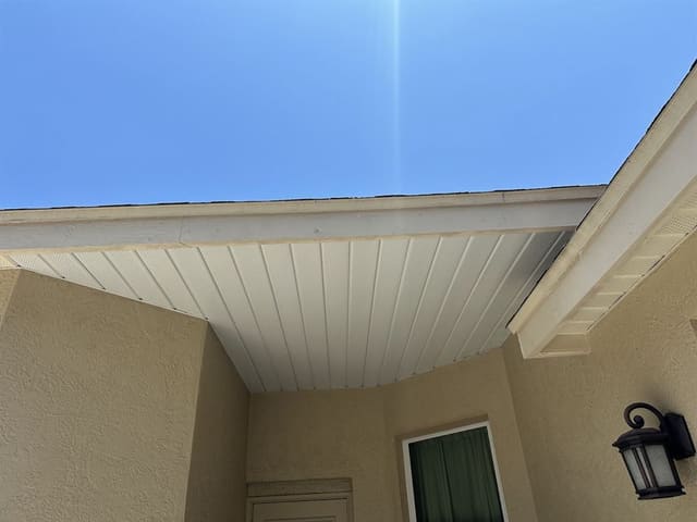 White vented soffit above a tan stucco entry with a black coach lamp.